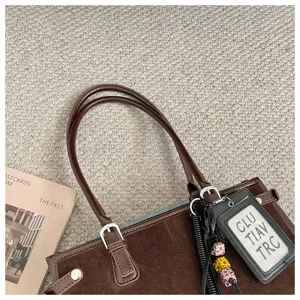 Brown suede tote bag detail view showing double handles and decorative charm accessory