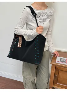 Vista detallada del bolso tote grande y suave negro con tachuelas azules y cinta marrón, casual.