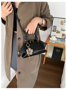 Sac à main élégant en cuir verni noir en forme de coquillage avec pendentif fleur.