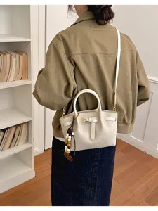 Vue détaillée du sac à main blanc élégant en motif crocodile avec nœud et charm de perles.