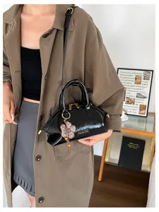 Vue détaillée du sac à main en cuir verni noir brillant avec charm fleur et bandoulière chic.