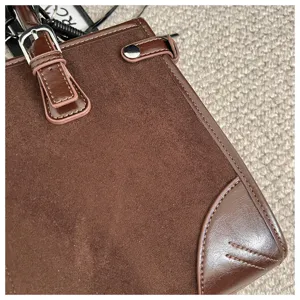 Close-up view of a brown suede and leather handbag showing fine stitching and metal hardware details.