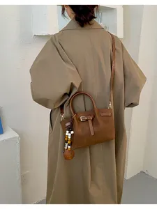 Vue détaillée du sac à main marron en cuir avec boucle, poignée et charmant pendentif de perles.