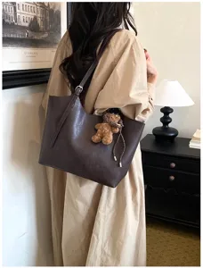 Vue détaillée d'un élégant sac cabas en cuir marron foncé avec charmant pendentif d'ours.
