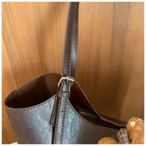Détail de sac cabas en cuir marron avec sangle réglable, boucle métallique et charm's ours.