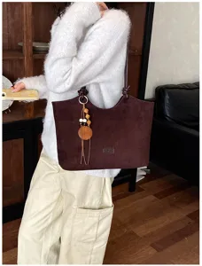 Gedetailleerd overzicht van een donkerbruine suède totebag met houten kralenhanger en schouderriem.