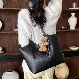 Élégant sac cabas en cuir noir pour femme, avec pendentif d'ours et bandoulière pratique.