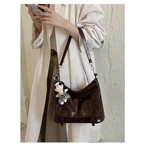 Detail view of the retro brown messenger bag with doll pendant, showing premium texture.
