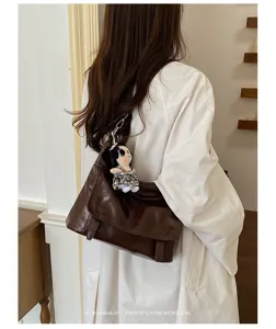 Retro brown glossy leather messenger bag worn on shoulder with cute doll pendant detail.