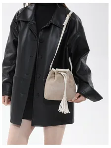 Detailed view of the stylish beige suede bucket bag with white strap and tassel drawstring.