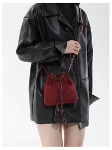 Close-up detail of dark red suede bucket bag with fringe and drawstring for autumn fashion.