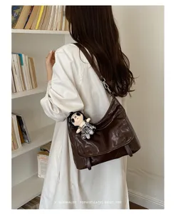 Brown patent leather shoulder messenger bag with cute doll charm and retro aesthetic design.
