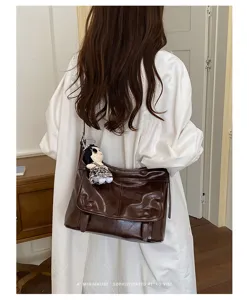 Detail view of the retro brown leather messenger shoulder bag featuring flap closure and cute charm.
