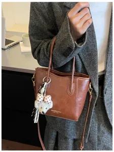 Dettaglio borsa tote in pelle marrone con grazioso ciondolo in peluche e doppi manici.