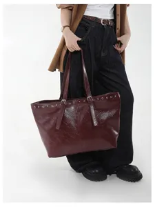 Detailansicht einer dunkelroten Ledertasche mit Tragegriffen und dekorativen Ösendetails.