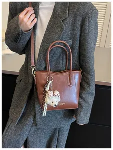 Borsa a secchiello in pelle marrone da donna, elegante borsa a tracolla con ciondolo cucciolo.