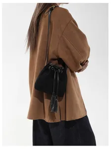 Detailed view of black suede bucket bag featuring drawstring closure and stylish tassel.