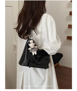 Detail view of a black patent leather messenger shoulder bag featuring a cute doll pendant.