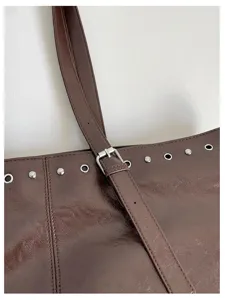Nahaufnahme einer braunen PU-Ledertasche mit metallischen Ösen und verstellbarem Riemen.