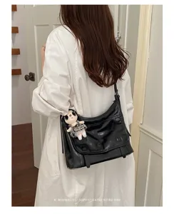 Detail view of stylish patent leather messenger shoulder bag with cute plush doll pendant.