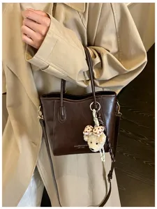 Elegante borsa a secchiello in pelle PU marrone da donna con ciondolo orsetto chic.