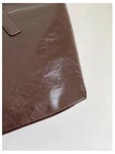 Nahaufnahme der Textur einer dunkelbraunen glänzenden Schultertasche mit feinen Nähten.