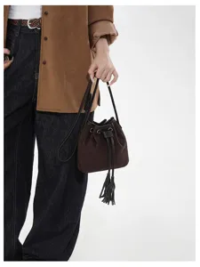Close-up of brown suede bucket bag featuring chic fringe, metal eyelets and drawstring.