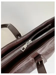 Nahaufnahme der dunkelbraunen, glänzenden Shopper-Tasche mit Reißverschluss und Beschlägen.