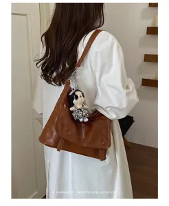 Brown retro leather shoulder bag detail, stylish messenger bag with cute doll pendant accent.