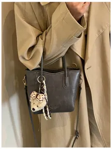 Vista di dettaglio di una borsa tote in pelle grigia con ciondolo orsetto di peluche e manici.