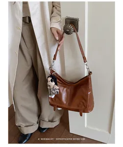 Detailed view of brown retro leather messenger shoulder bag with metal hardware and chic pendant.