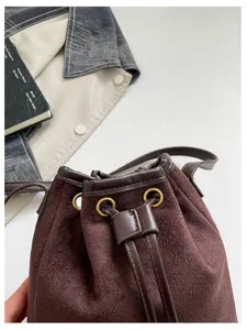 Close-up detail shot of dark brown suede bucket bag with metal eyelets and drawstring closure.