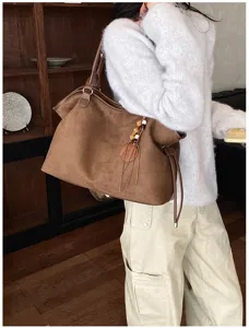 Retro brown suede tote bag with fringe charm and drawstring detail for casual daily commuter use.