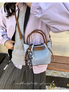 Detailed view of fashionable denim texture bucket handbag with brown leather trim and charm.