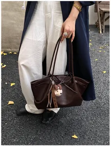 Close-up detail of a dark brown leather tote bag with shoulder straps and cute bear charm.