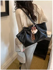 Detailed lifestyle shot of a stylish black leather tote bag featuring a cute bear plush pendant.