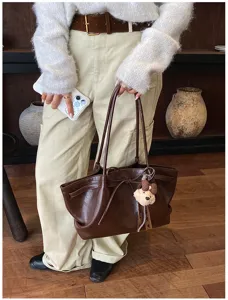 Detailed shot of retro brown leather tote bag with bow and cute bear pendant, stylish shoulder bag.