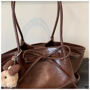 Brown vintage tote bag detail showing cute bowknot design and plush bear pendant accessory.
