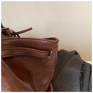 Close-up detail of the brown leather shoulder bag, highlighting texture and neat stitching work.