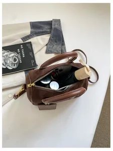 Detailansicht der braunen Wildleder Boston Handtasche mit geräumigem Innenraum und Accessoires.