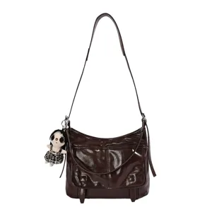 Donkerbruine glanzende leren schoudertas, retro messenger bag variant met schattige poppenhanger.