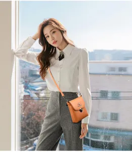 Stijlvolle oranje mini leren crossbody telefoontas gedragen door model in helder interieur.