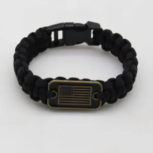 Detail view of black paracord survival bracelet with US flag metal tag and plastic buckle.