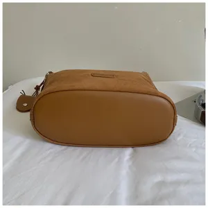 Brown suede bucket bag detail view showcasing smooth leather oval bottom and craftsmanship.