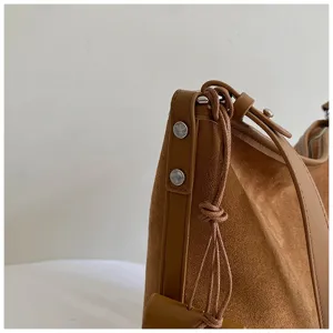 Close-up detail of brown suede shoulder bucket bag with leather straps and metal rivets.