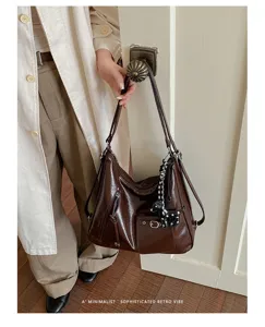 Detail shot of a dark brown patent leather tote bag with a cute dog charm and side zipper.