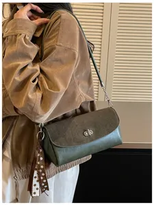 Detail view of stylish dark green shoulder bag with turn-lock and ribbon charm.