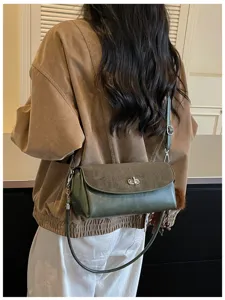 Detailed view of a dark green trendy shoulder bag with metal lock closure and adjustable strap.
