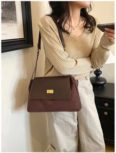 Close-up detail of brown suede and leather shoulder bag with chic gold twist lock and chain.