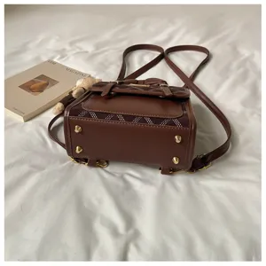 Detailed view of trendy brown mini backpack with buckle straps and metal studs on clean white bed.